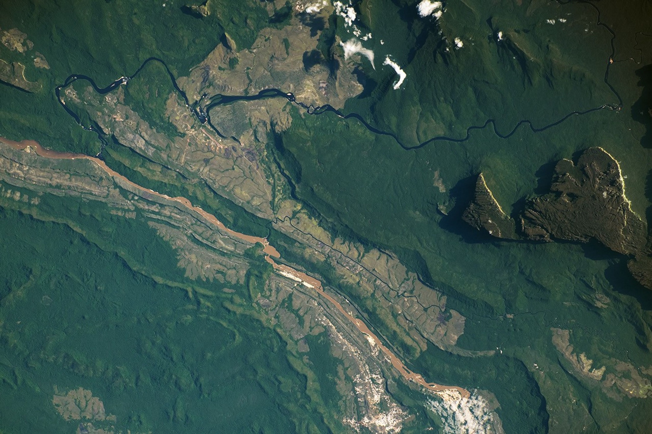 Astronaut photograph of rainforests, rivers, and table-top mountains surrounding Canaima in southeastern Venezuela.